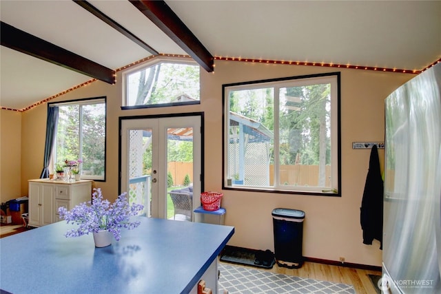 dining room featuring lofted ceiling with beams, a healthy amount of sunlight, french doors, and light wood finished floors
