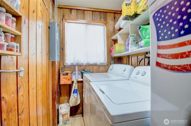 clothes washing area featuring washer and dryer, laundry area, wood walls, and electric panel