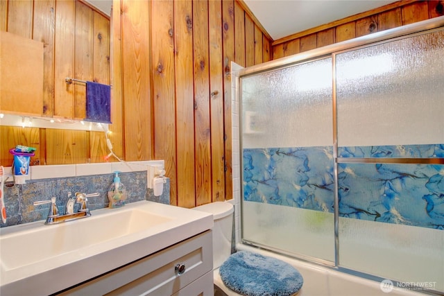 bathroom featuring vanity, wood walls, combined bath / shower with glass door, and toilet