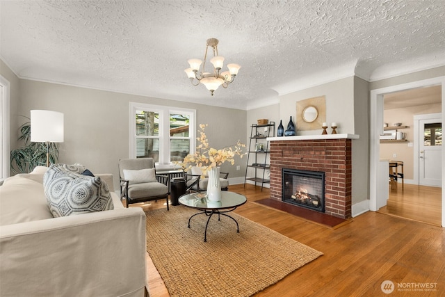 living room with wood finished floors, a textured ceiling, a brick fireplace, a chandelier, and baseboards