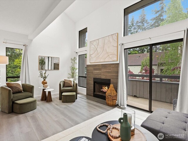 living room with a tiled fireplace, baseboards, high vaulted ceiling, and wood finished floors