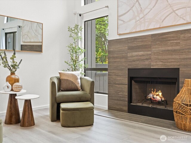 sitting room featuring baseboards, wood finished floors, and a warm lit fireplace