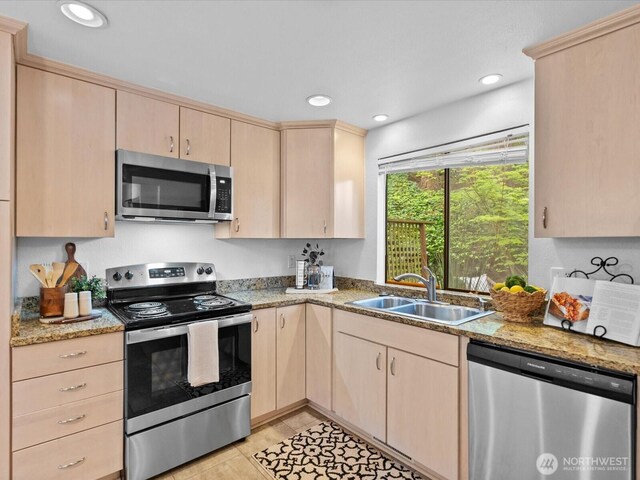 kitchen featuring light brown cabinetry, appliances with stainless steel finishes, light stone countertops, and a sink