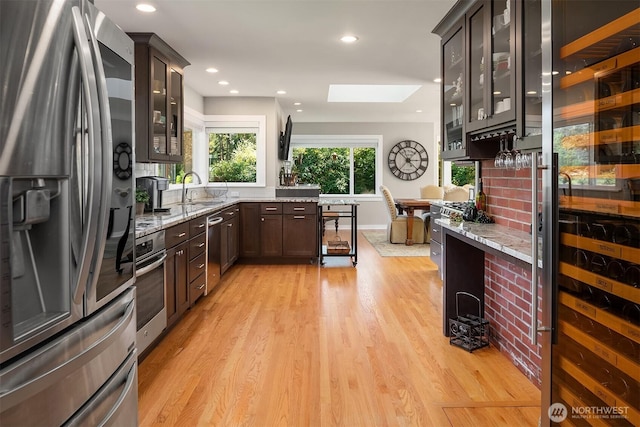 kitchen featuring appliances with stainless steel finishes, a sink, light wood-style floors, light stone countertops, and dark brown cabinets