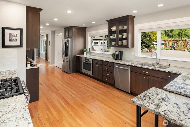 kitchen featuring stainless steel appliances, a sink, dark brown cabinets, light wood-style floors, and recessed lighting