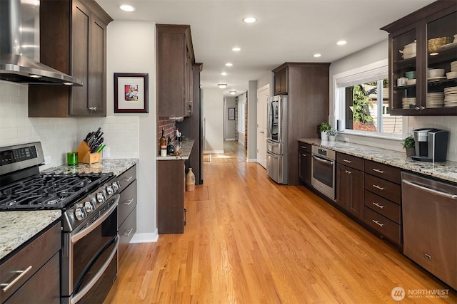 kitchen featuring wall chimney range hood, stainless steel appliances, baseboards, dark brown cabinetry, and recessed lighting