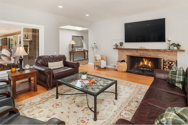 living area with wood finished floors, a lit fireplace, recessed lighting, and baseboards