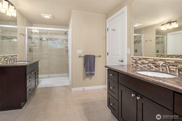 full bathroom featuring a stall shower, tile patterned floors, baseboards, two vanities, and decorative backsplash