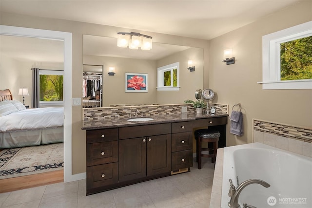 ensuite bathroom featuring plenty of natural light, tile patterned floors, a bath, and decorative backsplash