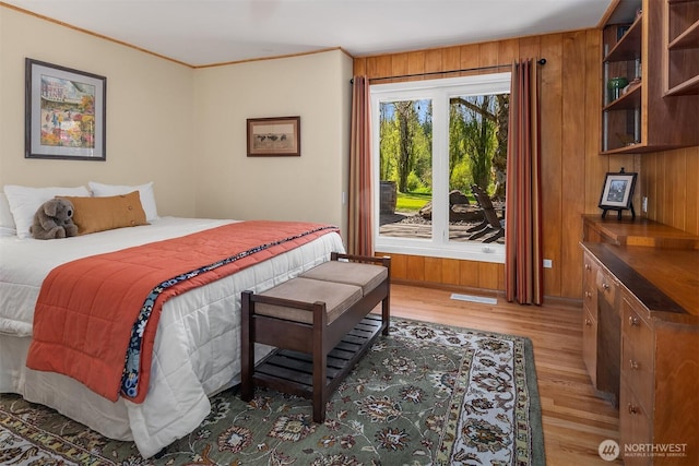 bedroom with light wood finished floors, crown molding, and wooden walls