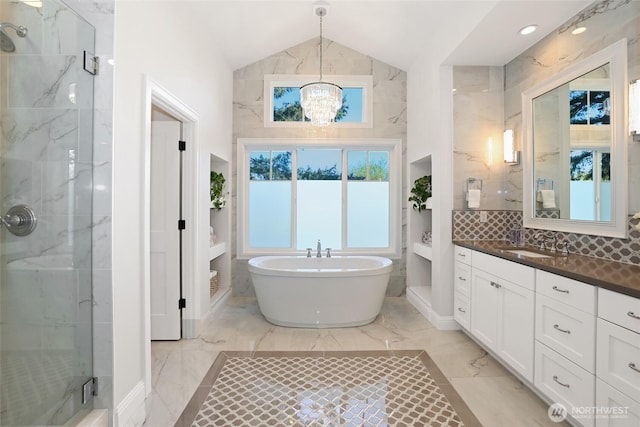 bathroom with a chandelier, marble finish floor, lofted ceiling, a marble finish shower, and a soaking tub