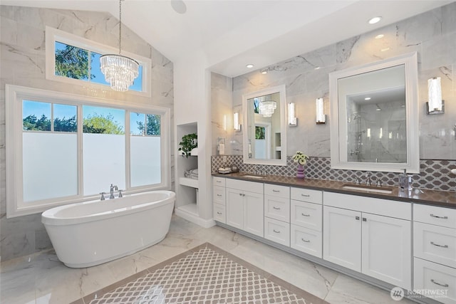 full bath featuring double vanity, marble finish floor, a chandelier, a soaking tub, and a sink