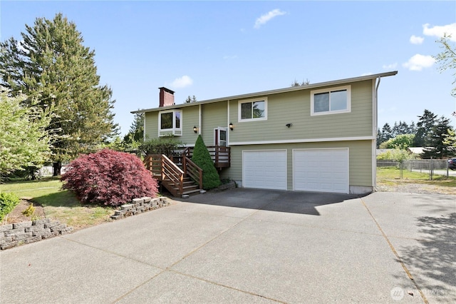 bi-level home featuring stairway, concrete driveway, an attached garage, a chimney, and fence