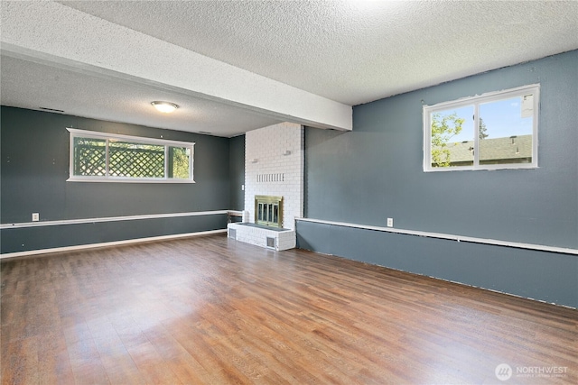 unfurnished living room with wood finished floors, a textured ceiling, and a brick fireplace