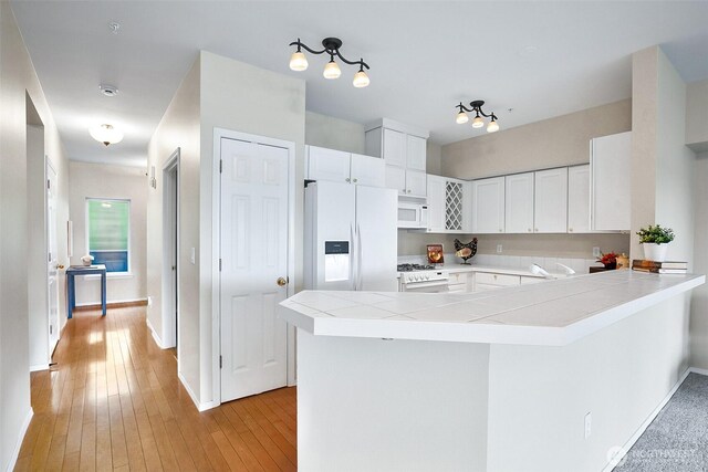 kitchen with tile countertops, white cabinets, a peninsula, white appliances, and light wood-style flooring