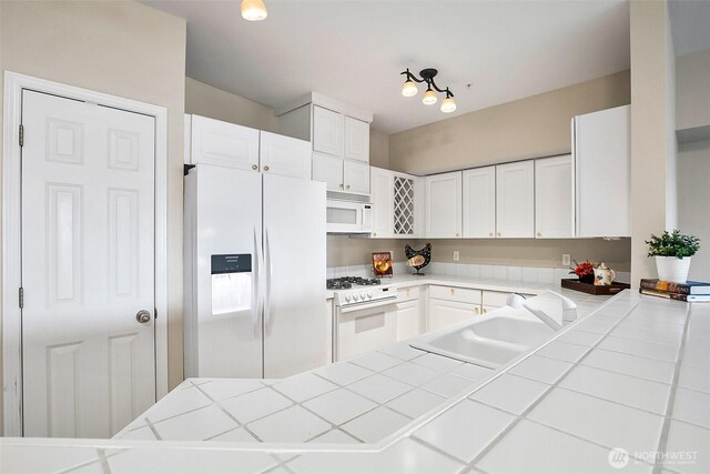 kitchen featuring a sink, white cabinets, a peninsula, tile counters, and white appliances