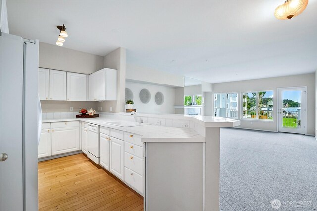 kitchen with white cabinets, a sink, white appliances, light countertops, and a peninsula