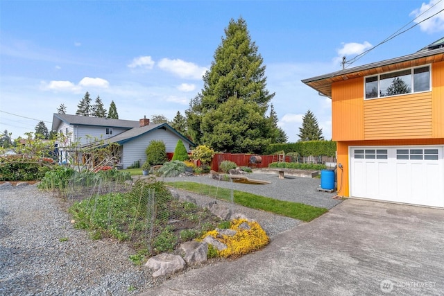 view of yard featuring driveway, fence, an attached garage, and a vegetable garden