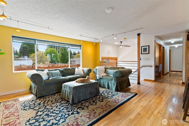 living area featuring a textured ceiling, wood finished floors, a ceiling fan, baseboards, and track lighting