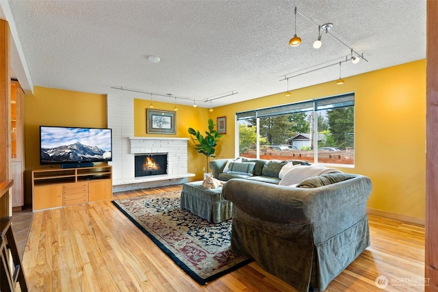 living area with track lighting, hardwood / wood-style flooring, a textured ceiling, and a lit fireplace