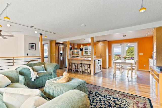 living room with a textured ceiling, light wood-style flooring, a ceiling fan, and track lighting