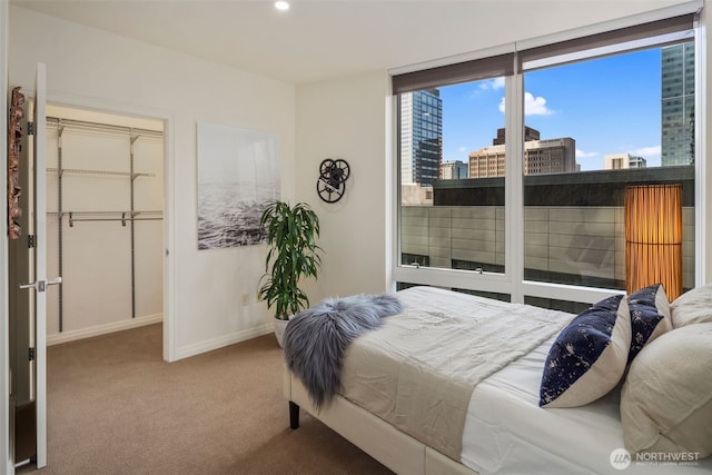 bedroom featuring baseboards, recessed lighting, a city view, carpet floors, and a walk in closet