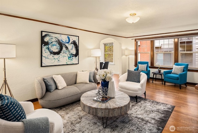 living room with arched walkways, crown molding, and wood finished floors
