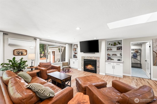 living room featuring an AC wall unit, a skylight, light wood-style floors, a tile fireplace, and baseboards