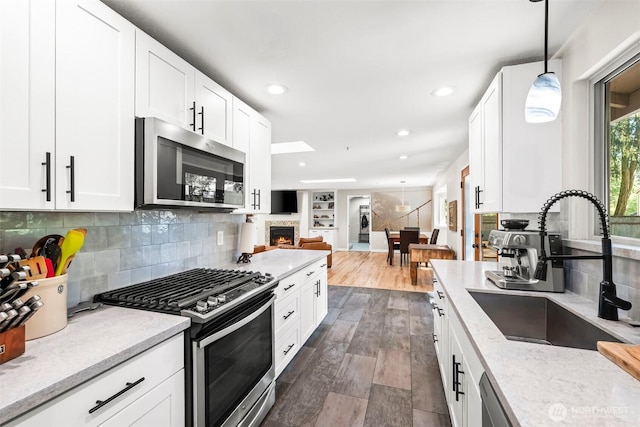 kitchen featuring stainless steel appliances, a sink, a lit fireplace, open floor plan, and white cabinets