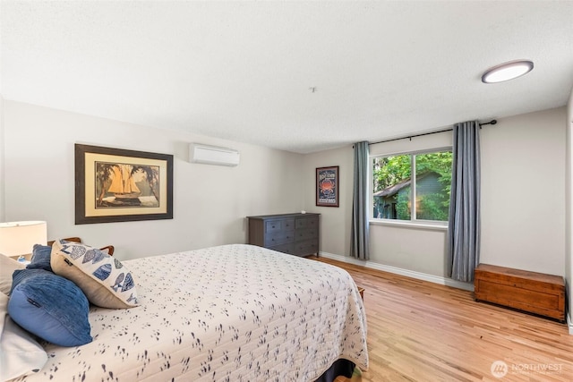 bedroom with an AC wall unit, light wood finished floors, and baseboards
