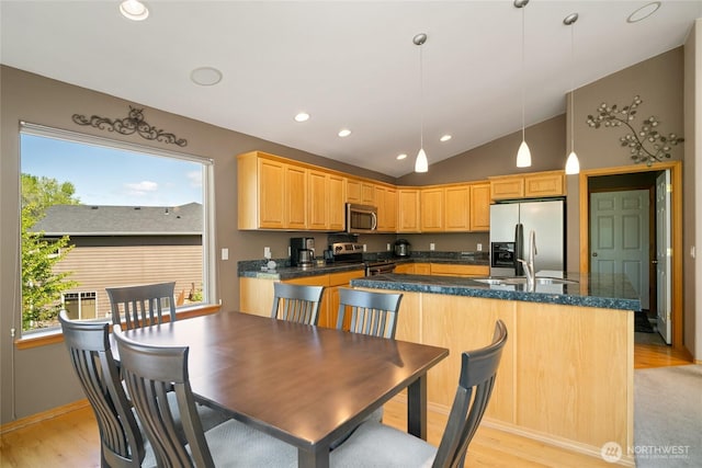 kitchen featuring stainless steel appliances, vaulted ceiling, dark countertops, and light wood-style flooring