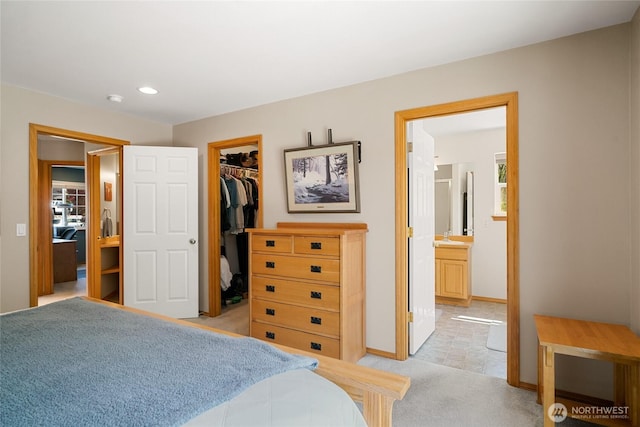 bedroom with light carpet, ensuite bathroom, baseboards, a spacious closet, and a closet