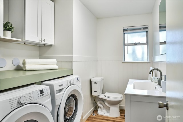 clothes washing area with washing machine and clothes dryer, wainscoting, and wood finished floors