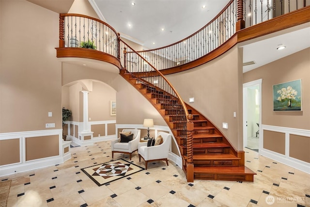 stairway featuring arched walkways, a decorative wall, a towering ceiling, and decorative columns