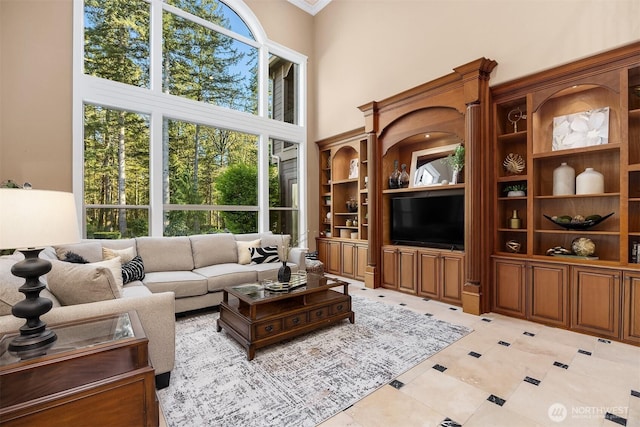 living room featuring light tile patterned flooring, a towering ceiling, ornamental molding, and built in features