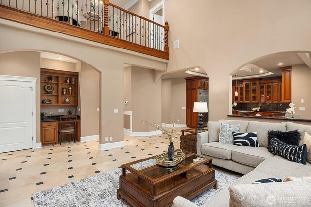 living area featuring arched walkways, baseboards, a towering ceiling, and light floors