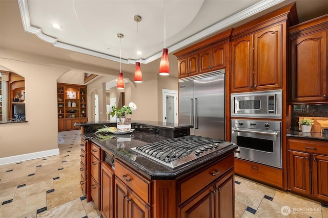 kitchen featuring built in appliances, a kitchen island, dark stone counters, and hanging light fixtures