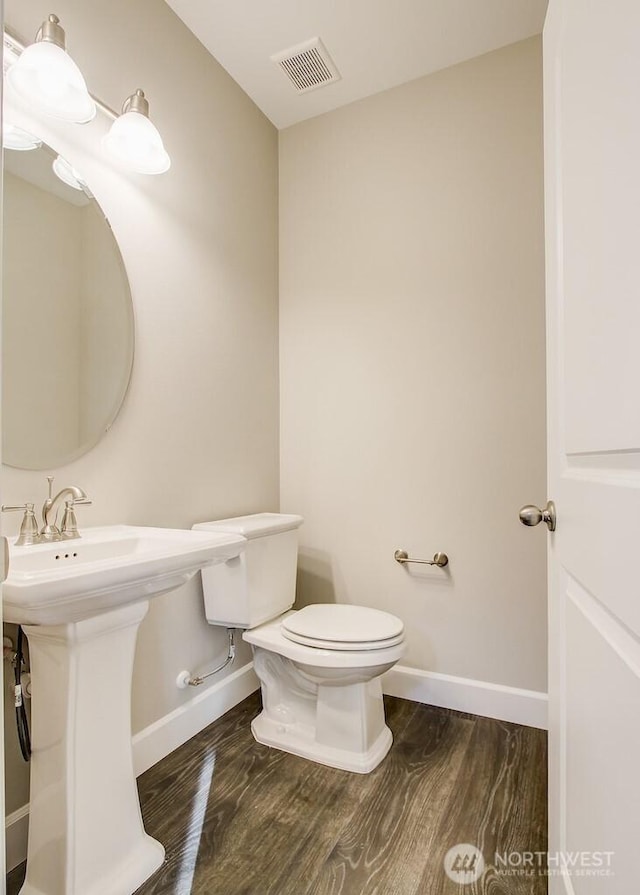 half bath with a sink, toilet, visible vents, baseboards, and wood finished floors