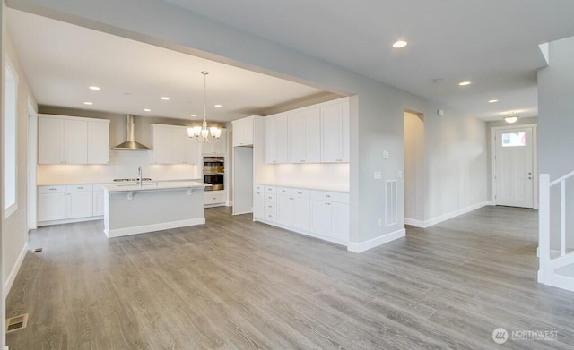 kitchen with recessed lighting, a notable chandelier, wall chimney exhaust hood, white cabinetry, and double oven
