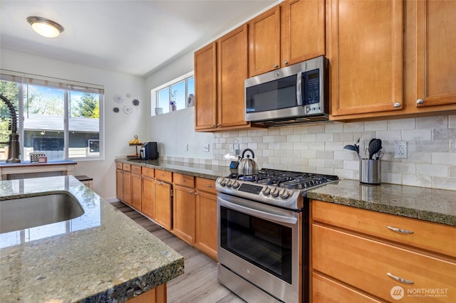 kitchen featuring brown cabinets, stainless steel appliances, stone countertops, light wood-style floors, and decorative backsplash
