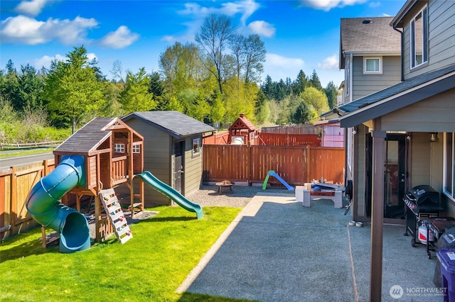view of jungle gym featuring a fenced backyard, a patio, an outdoor fire pit, and a lawn