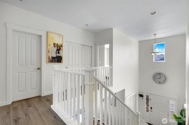hallway featuring baseboards, wood finished floors, recessed lighting, and an upstairs landing
