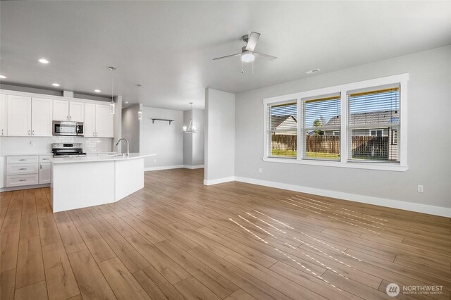 unfurnished living room with a ceiling fan, a sink, baseboards, recessed lighting, and light wood-style flooring