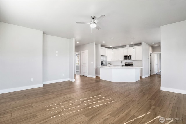 unfurnished living room with wood finished floors, baseboards, ceiling fan, recessed lighting, and a sink