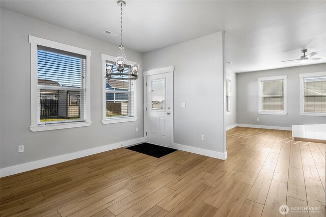 entrance foyer with baseboards, ceiling fan with notable chandelier, wood finished floors, and visible vents