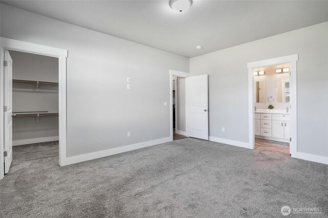 unfurnished bedroom featuring a closet, baseboards, a walk in closet, connected bathroom, and carpet