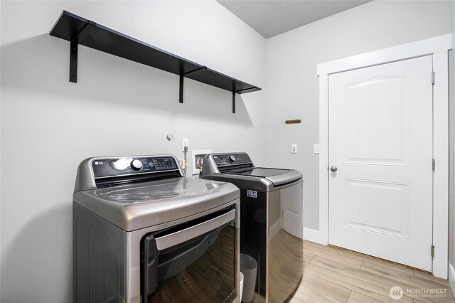 clothes washing area featuring baseboards, separate washer and dryer, laundry area, and light wood-style flooring