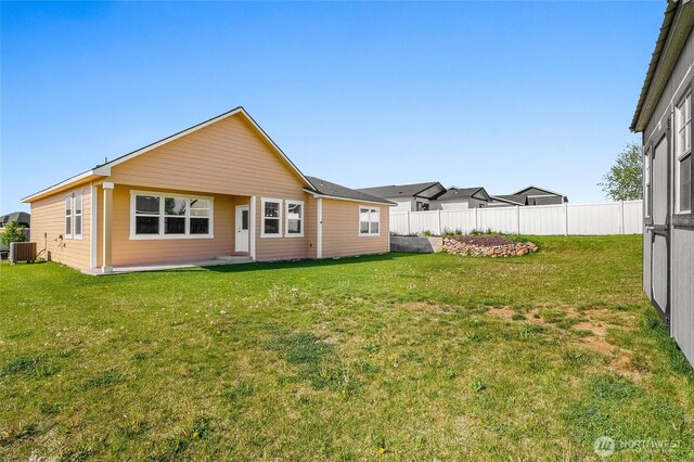 back of house with central air condition unit, fence, and a yard