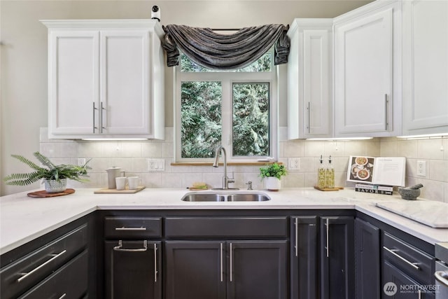 kitchen with a sink, white cabinetry, light stone counters, and tasteful backsplash