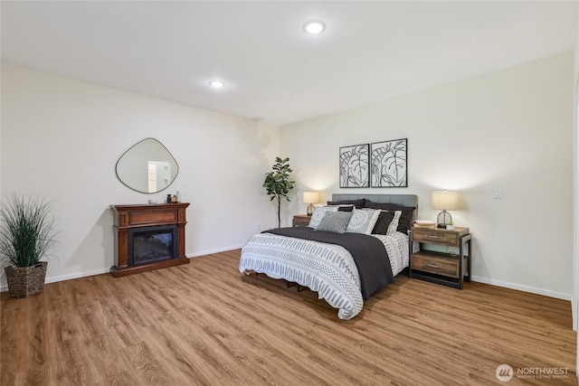 bedroom featuring baseboards, a glass covered fireplace, wood finished floors, and recessed lighting